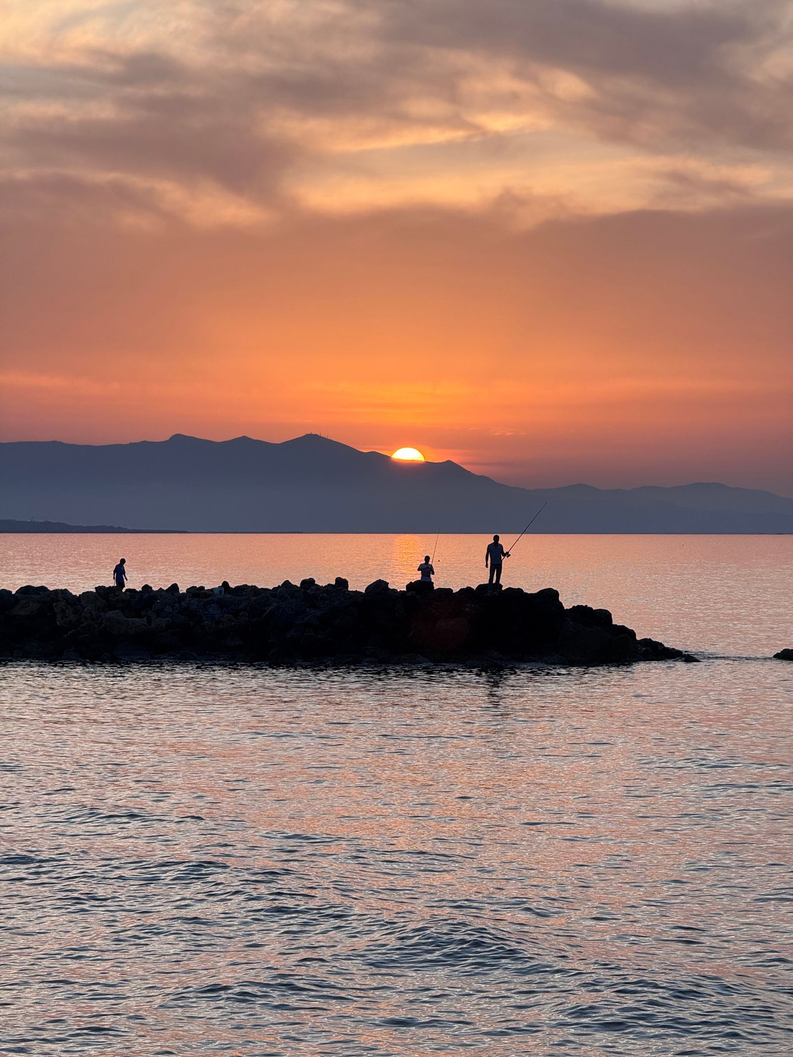 Gün batımında kayalık Akdeniz kıyısında balıkçı silüetleri
